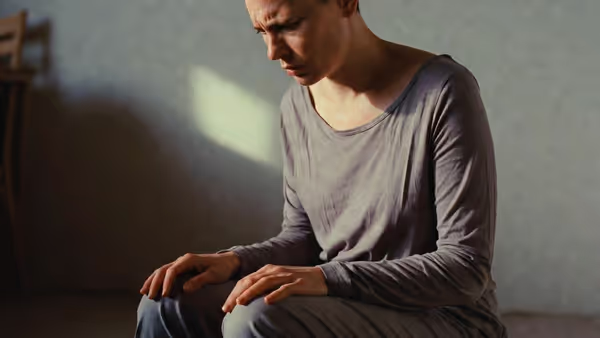 Person sitting indoors looking down with self-critical expression